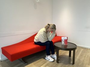 Kopfschmerzen & Schwindel? Erfahren Sie, wann ein Kopf-MRT sinnvoll ist, welche Ursachen abgeklärt werden und wie die Untersuchung abläuft.Bild von Patientin in der Radiologie, die sich den Kopf hält und auf einer roten Couch sitzt